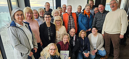 DRK Akkordeonorchester Der DRK Akkordeonorchester steht lächelnd zusammen vor einer Fensterfront